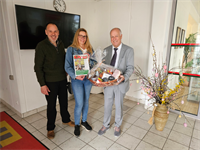 Gewinnerin mit Zeitung in der Hand, Sponsor und Bürgermeister der einen Osterkorb hält